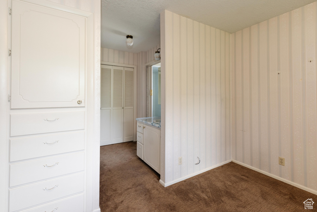 Unfurnished bedroom with dark carpet, a textured ceiling, and wallpapered walls
