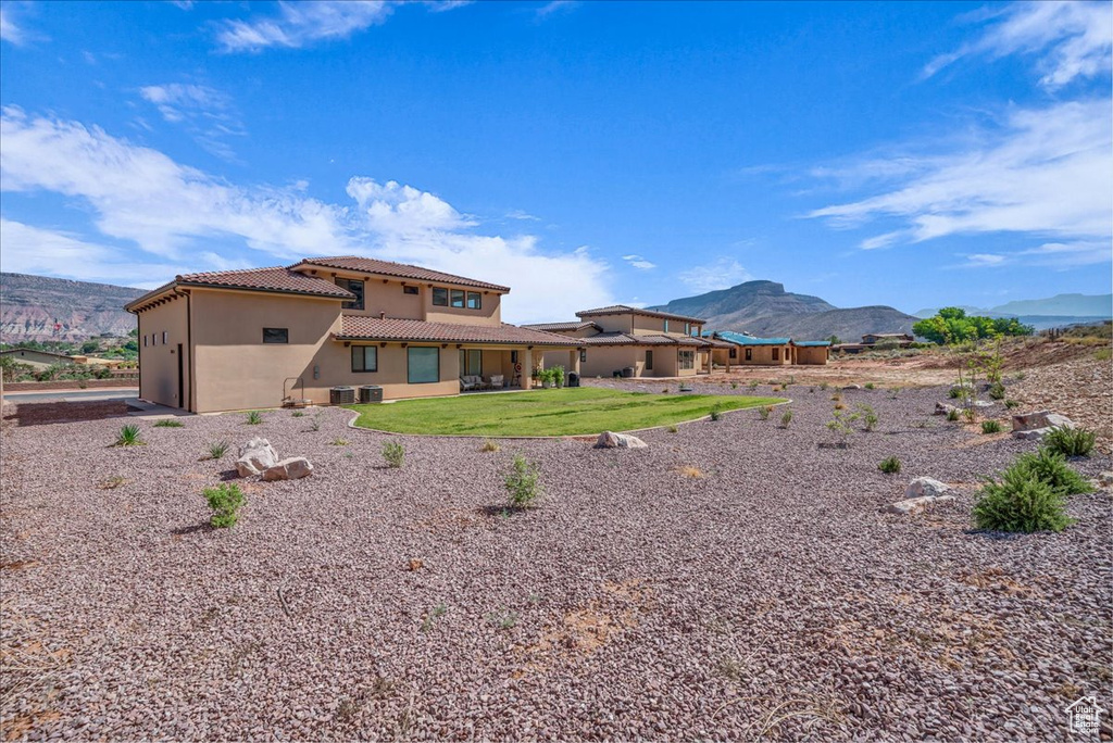 Back of house with a tiled roof, stucco siding, a mountain view, and a lawn