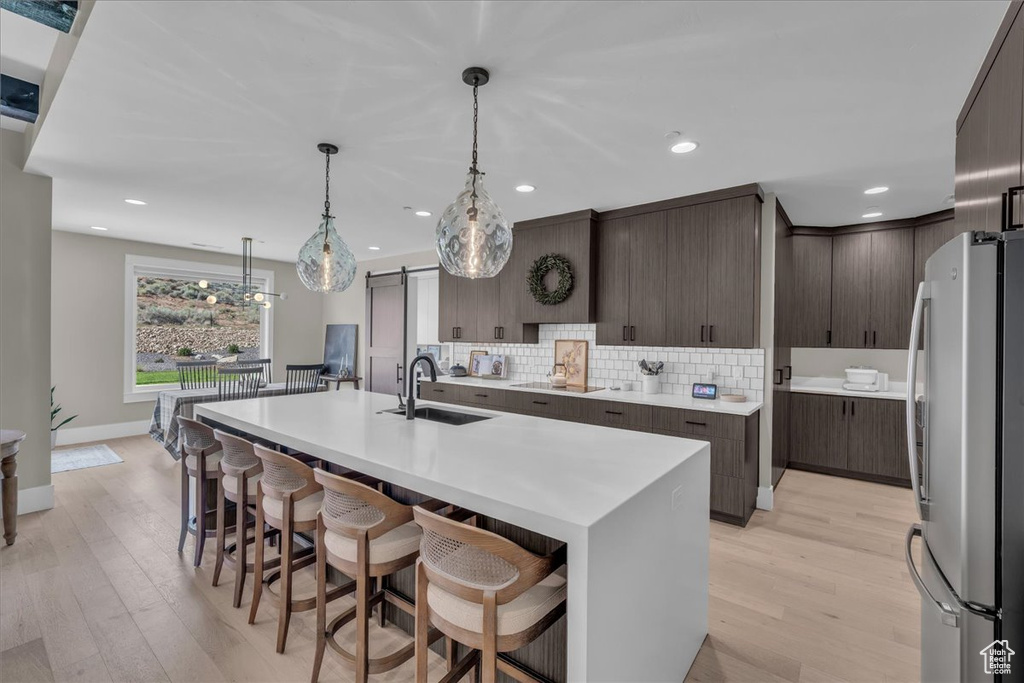 Kitchen with freestanding refrigerator, light wood-style flooring, dark brown cabinets, decorative backsplash, and a breakfast bar area