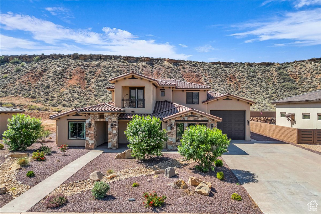 Mediterranean / spanish-style home with concrete driveway, stucco siding, a tiled roof, stone siding, and a mountain view