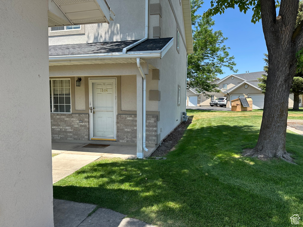 Doorway to property with stucco siding, a lawn, and roof with shingles