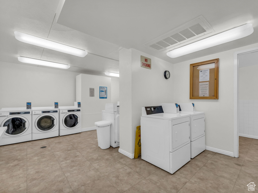 Community laundry room with washing machine and dryer and light tile patterned floors