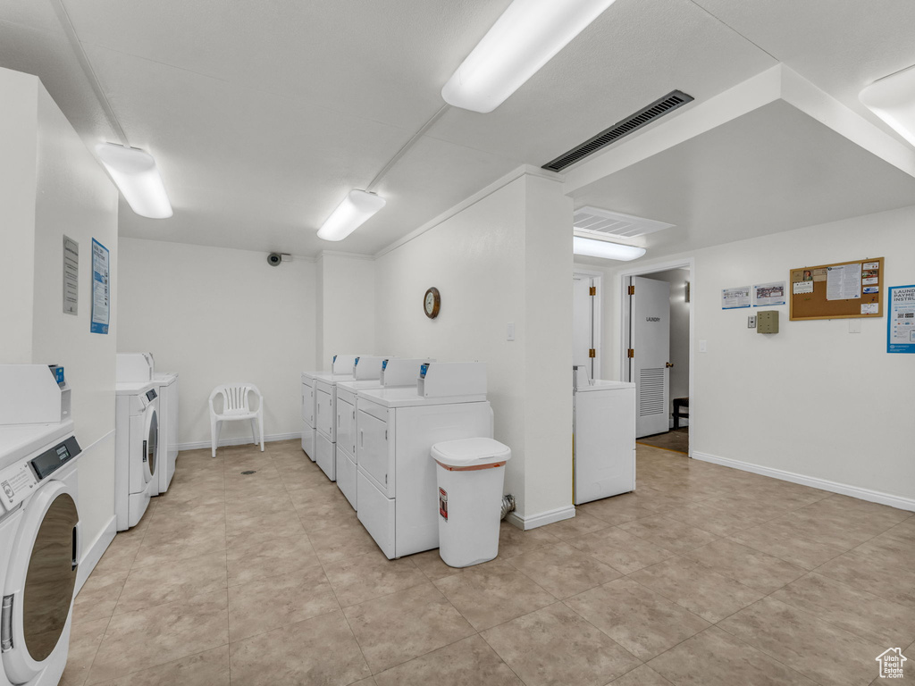 Shared laundry with washing machine and clothes dryer and light tile patterned flooring