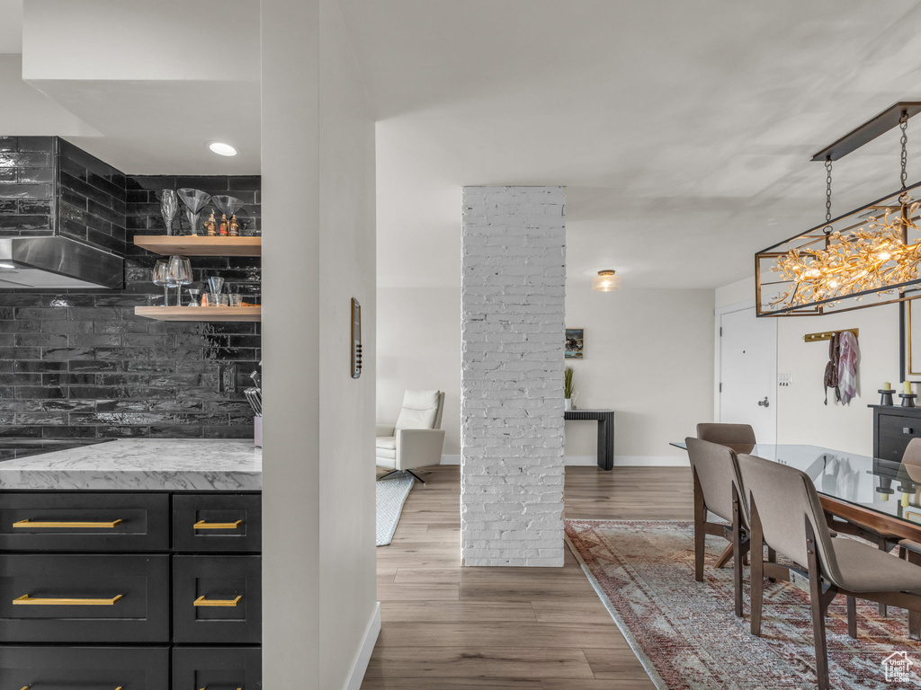 Indoor dry bar featuring decorative columns, extractor fan, wood finished floors, tasteful backsplash, and a chandelier