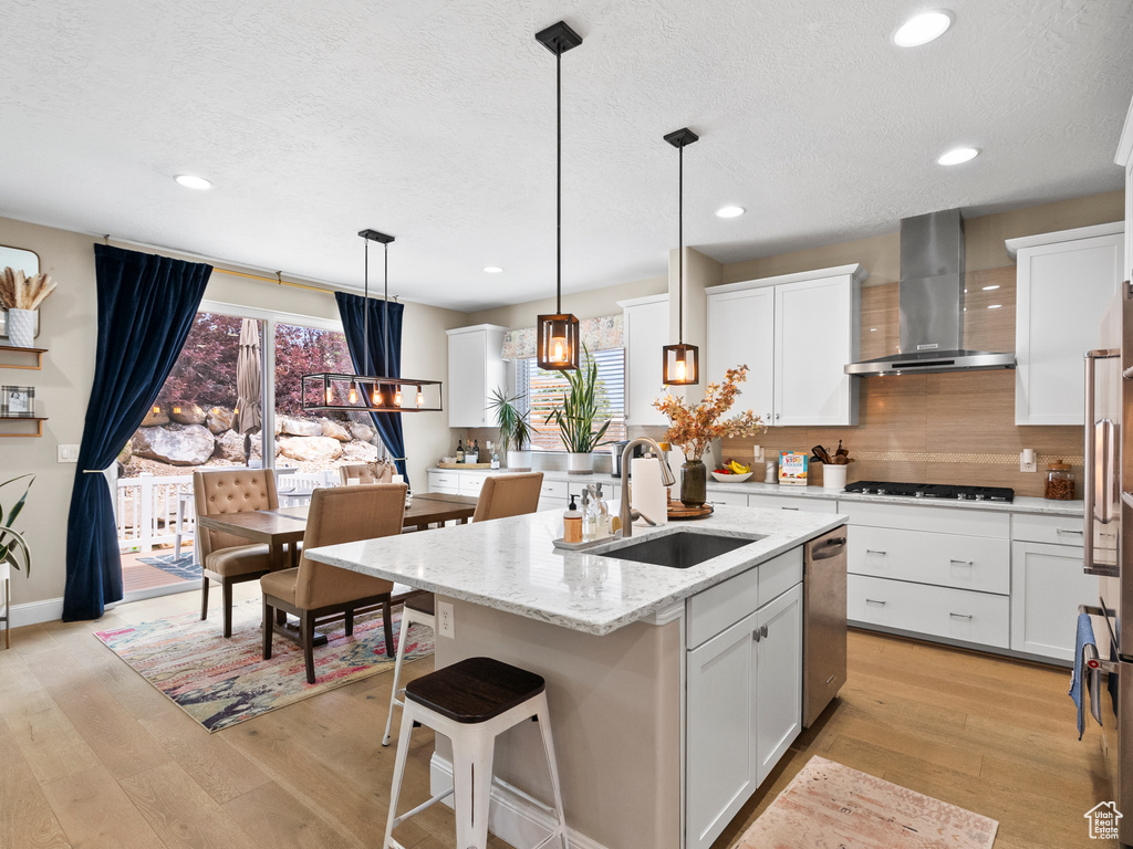 Kitchen with wall chimney range hood, light wood finished floors, a textured ceiling, gas cooktop, and tasteful backsplash