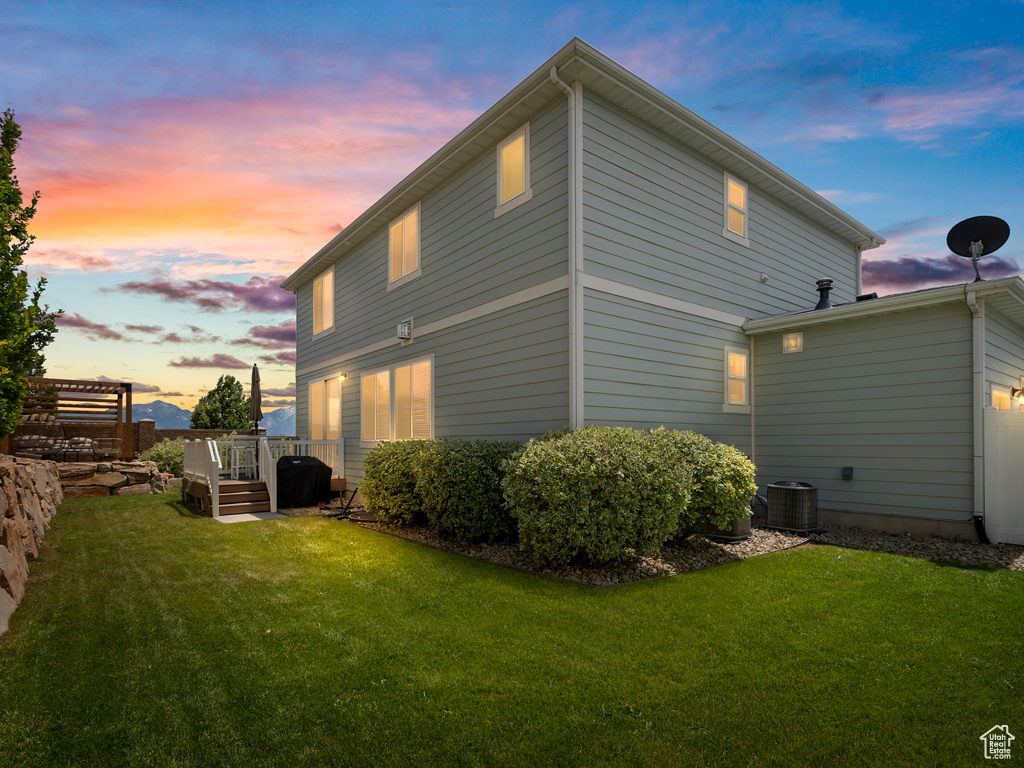 Back of house at dusk with a lawn and a deck