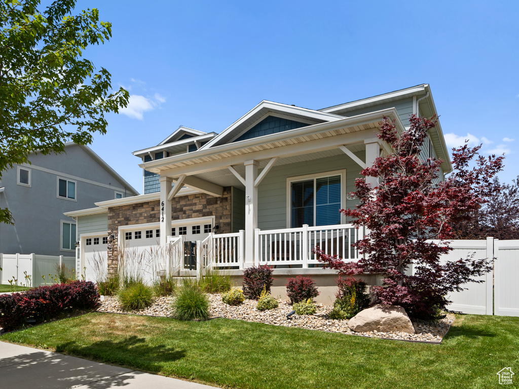 View of front facade with a porch, a garage, and stone siding