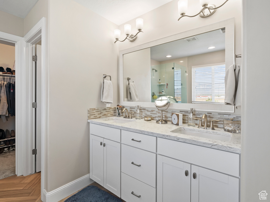 Bathroom with a walk in closet, double vanity, a stall shower, and backsplash
