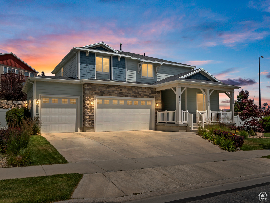 View of front of home featuring a porch, driveway, an attached garage, and stone siding