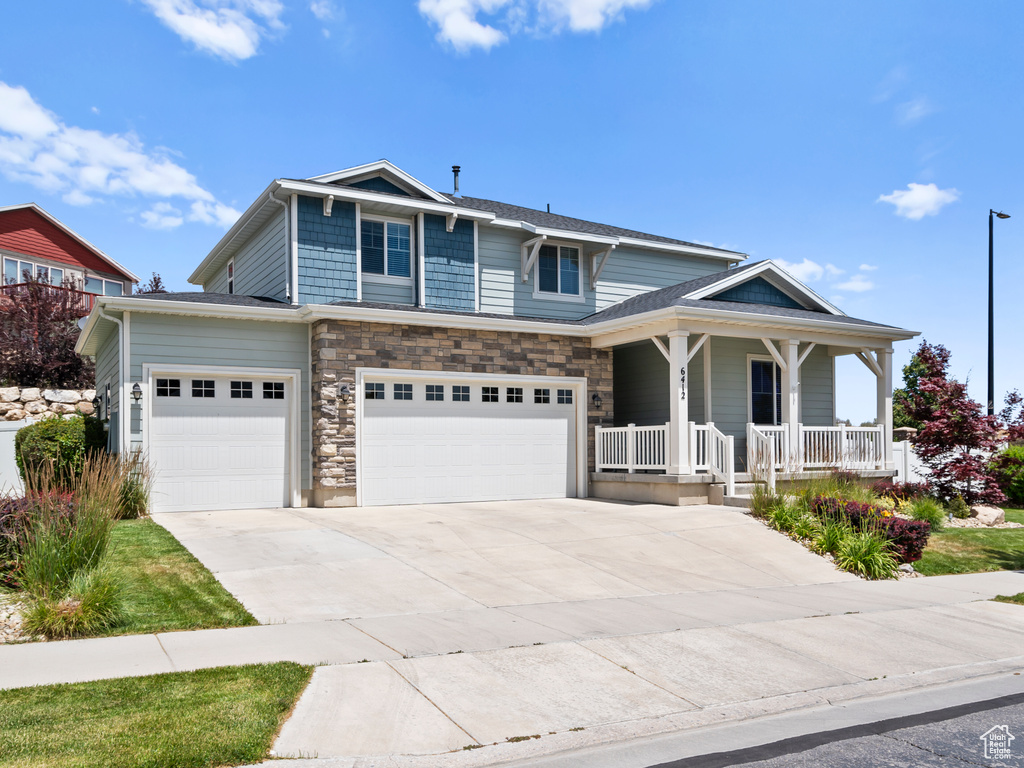 View of front of house featuring a porch, concrete driveway, a garage, and stone siding