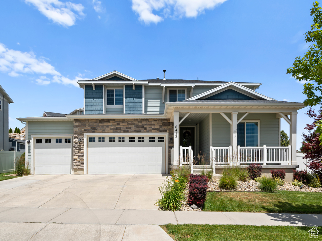 View of front of home featuring a porch, concrete driveway, a garage, and stone siding