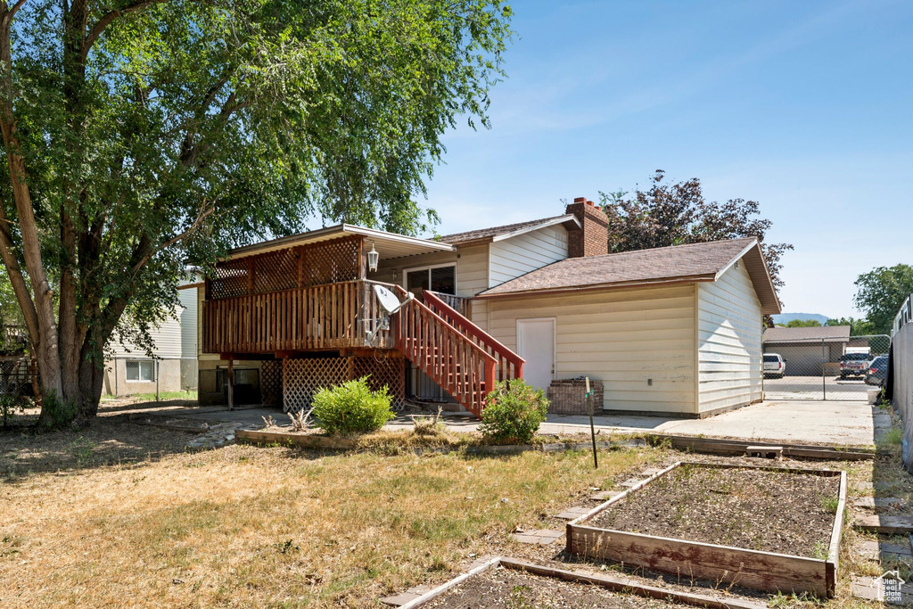 Rear view of house featuring a garden, a wooden deck, stairs, a chimney, and roof with shingles