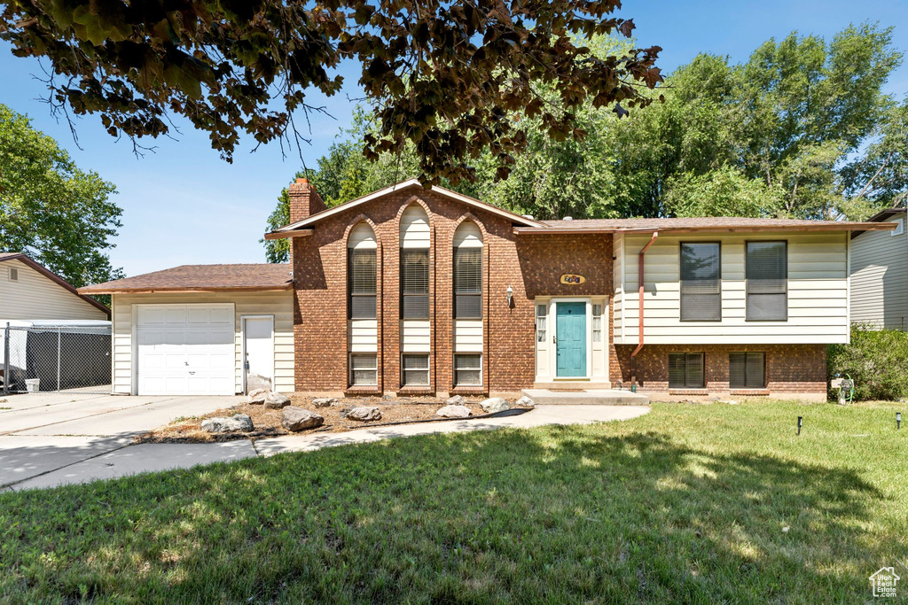 Split foyer home featuring an attached garage, brick siding, a front lawn, and a chimney