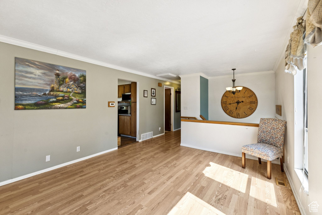 Living area with light wood finished floors, crown molding, and a chandelier