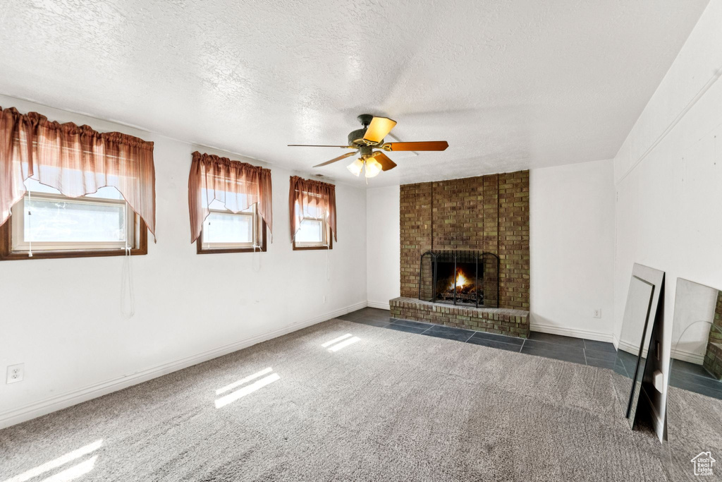 Unfurnished living room with ceiling fan, a textured ceiling, plenty of natural light, a fireplace, and carpet flooring