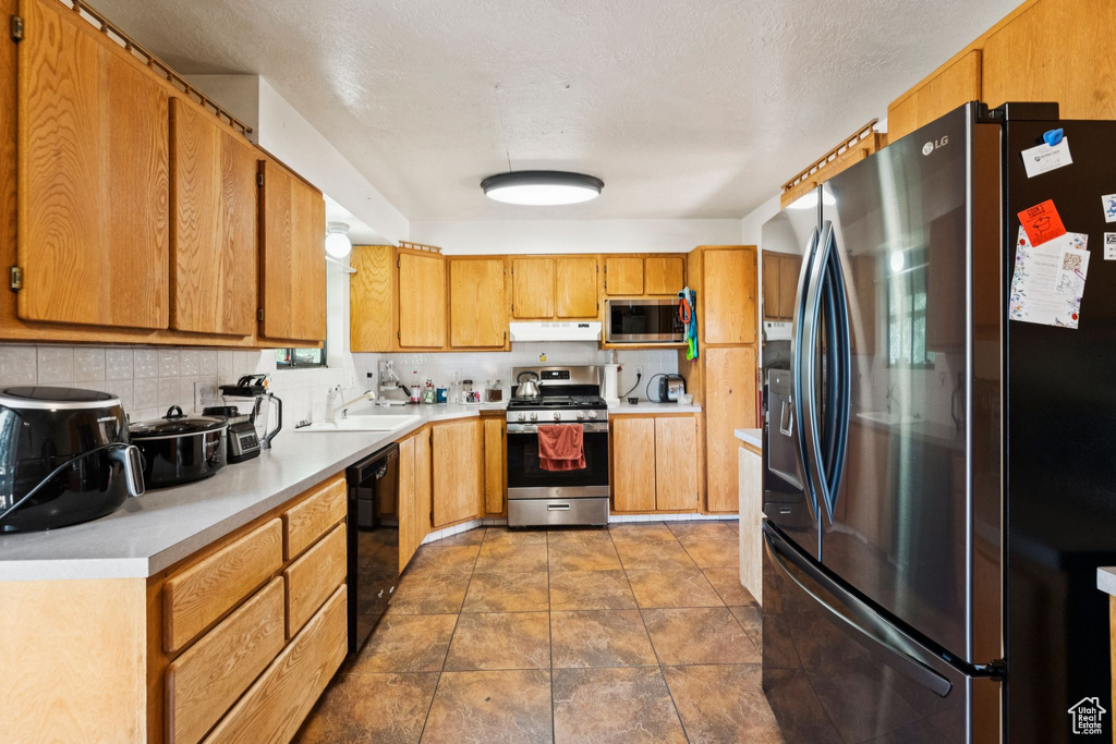 Kitchen featuring appliances with stainless steel finishes, ventilation hood, light countertops, decorative backsplash, and brown cabinets