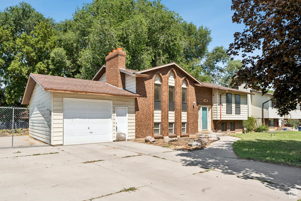 Split foyer home featuring a chimney, driveway, a garage, brick siding, and a shingled roof
