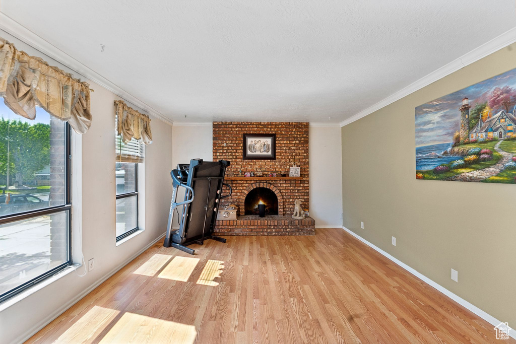 Unfurnished living room with light wood finished floors, ornamental molding, and a brick fireplace