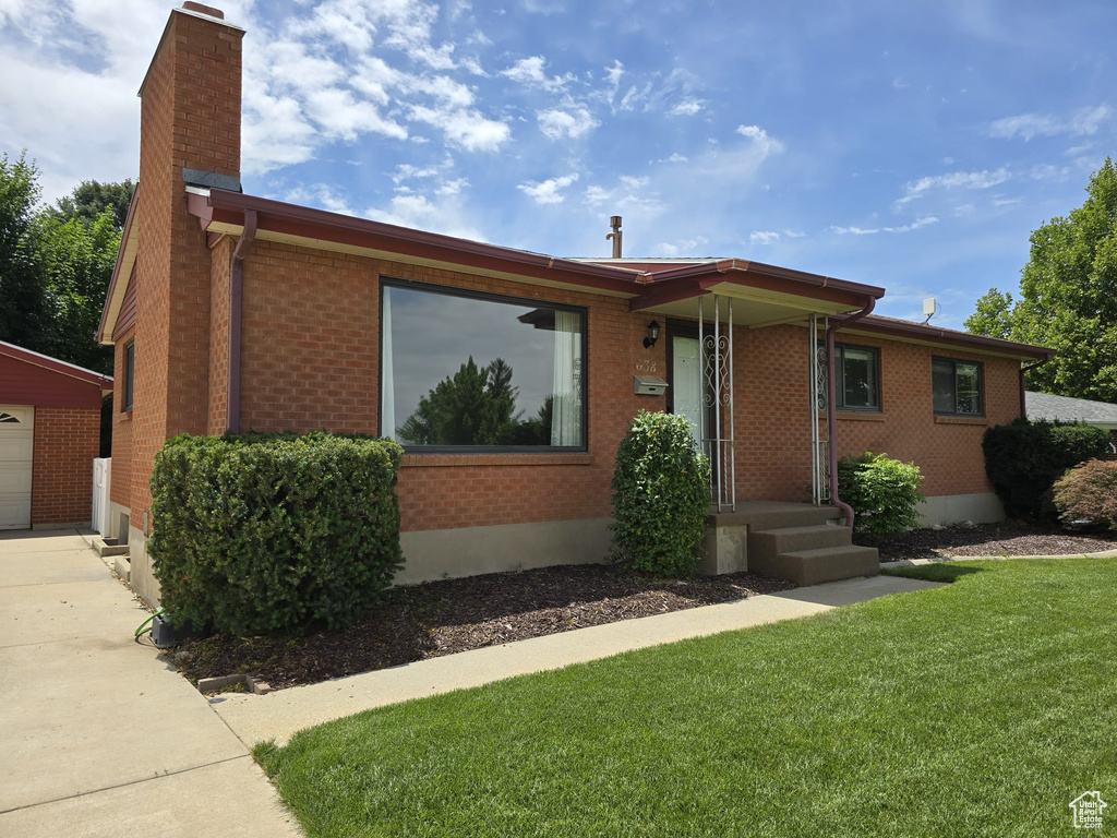 Ranch-style house with a chimney, a front yard, brick siding, a garage, and an outbuilding