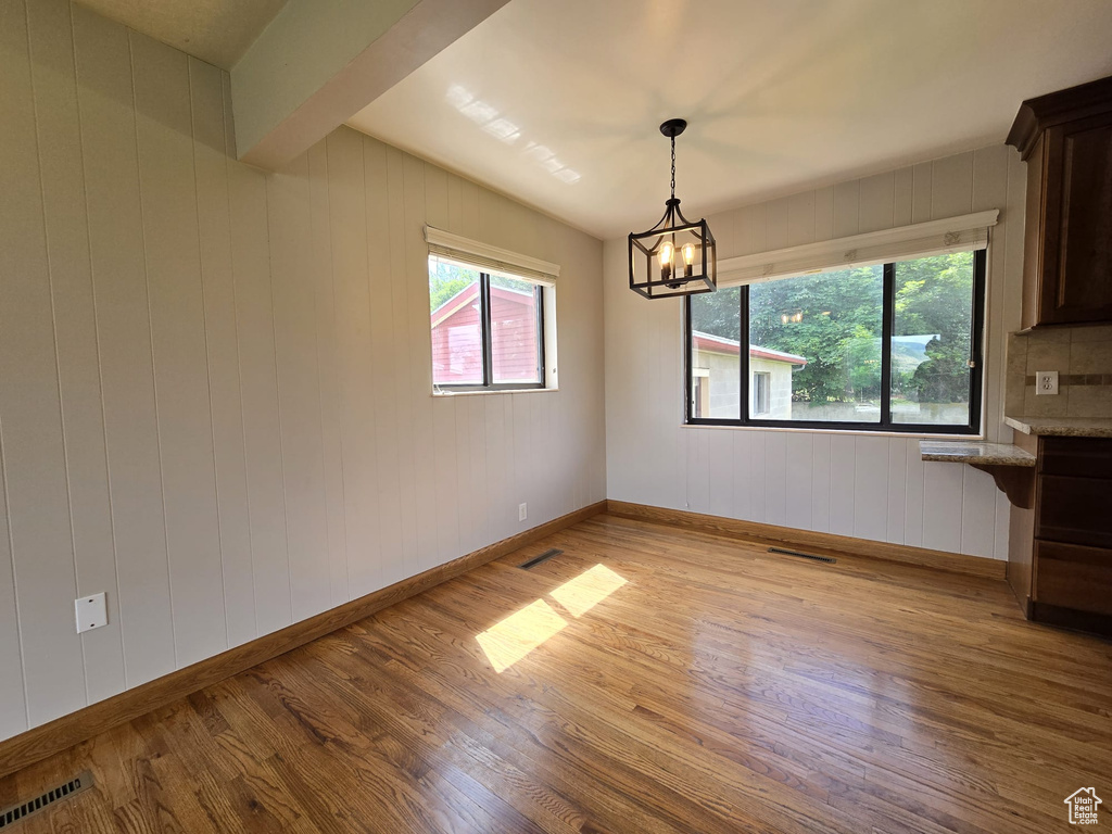Unfurnished dining area featuring light wood finished floors, plenty of natural light, a chandelier, and wood walls