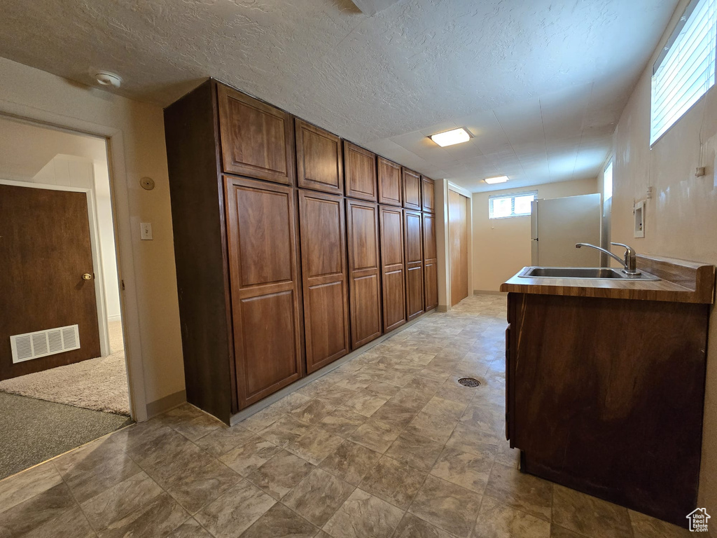 Kitchen featuring freestanding refrigerator, a textured ceiling, and brown cabinetry