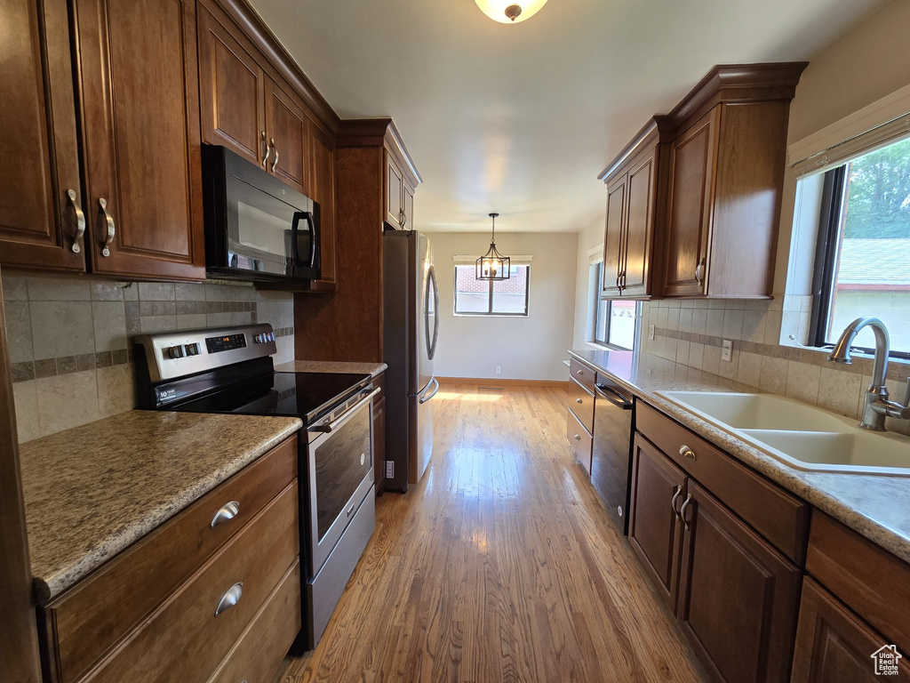 Kitchen featuring stainless steel appliances, light wood-type flooring, tasteful backsplash, and pendant lighting
