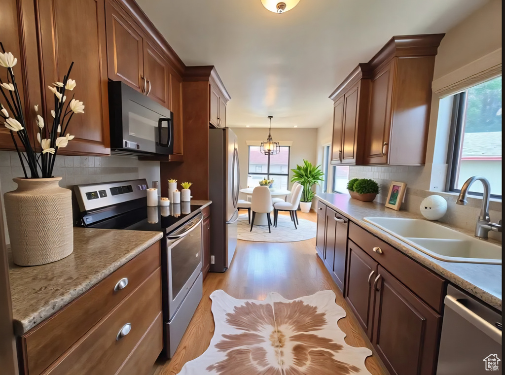 Kitchen featuring appliances with stainless steel finishes, light wood-type flooring, a chandelier, and backsplash