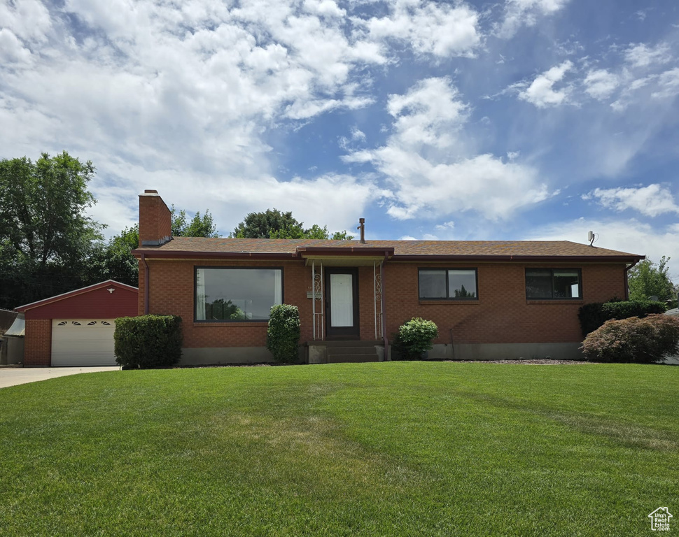 Single story home with brick siding, a chimney, a front yard, and concrete driveway