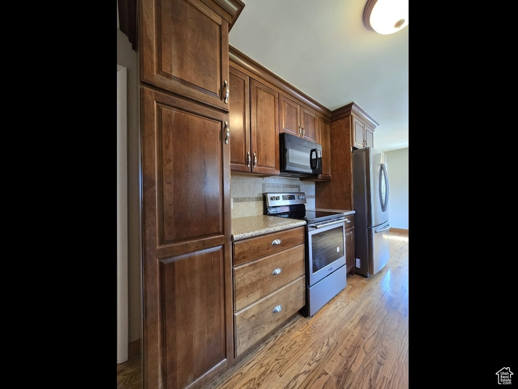 Kitchen with stainless steel appliances, backsplash, light wood-type flooring, and light countertops