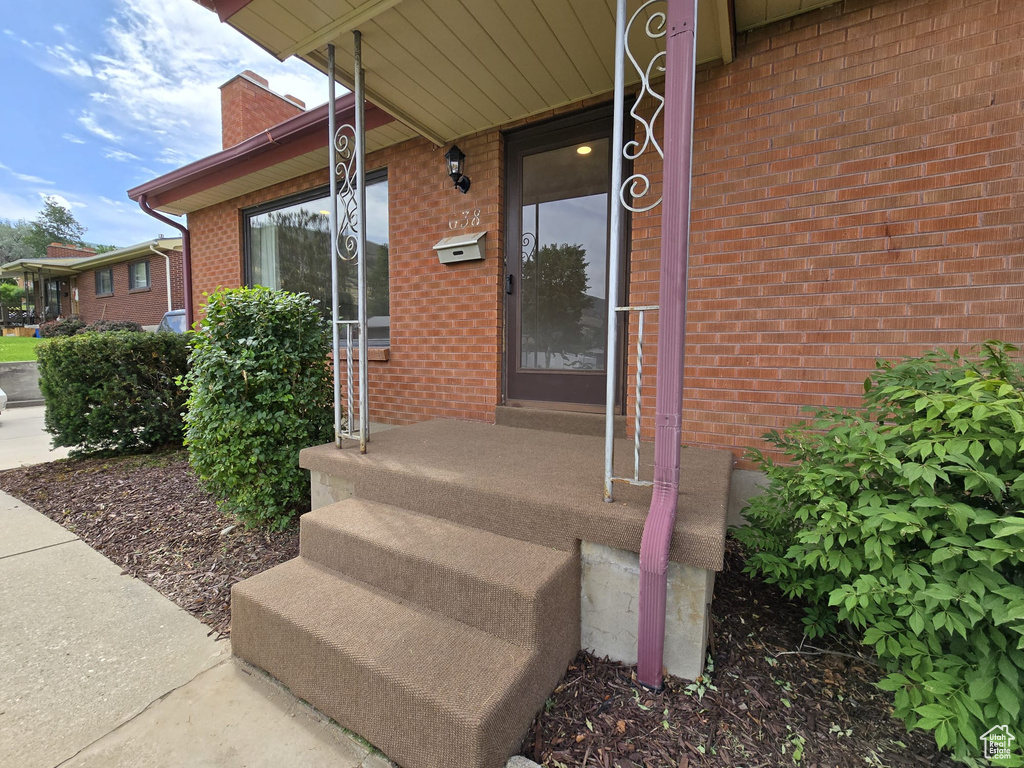 View of exterior entry with brick siding, a chimney, and a porch