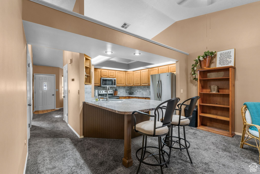 Kitchen with appliances with stainless steel finishes, open shelves, dark colored carpet, a kitchen breakfast bar, and vaulted ceiling