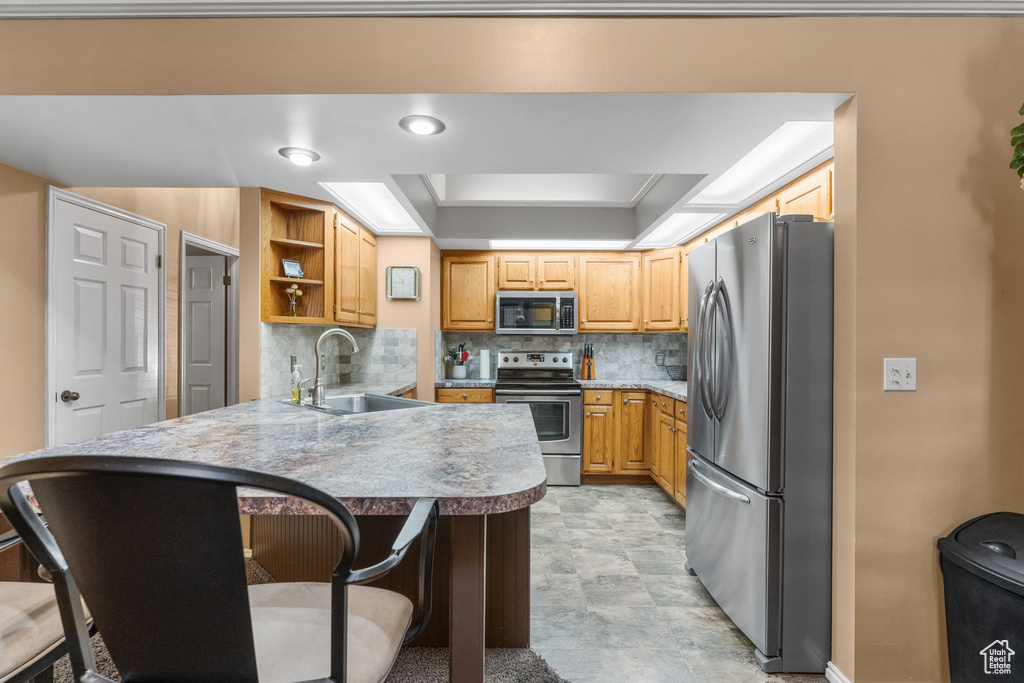Kitchen featuring stainless steel appliances, a peninsula, a breakfast bar area, open shelves, and backsplash