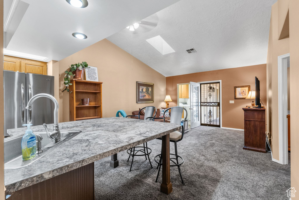 Kitchen featuring freestanding refrigerator, a skylight, vaulted ceiling, carpet flooring, and open floor plan