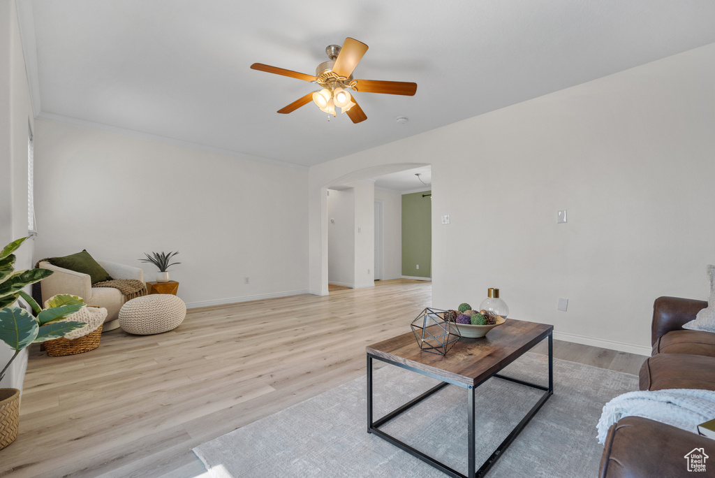Living room featuring arched walkways, light wood-style floors, and a ceiling fan