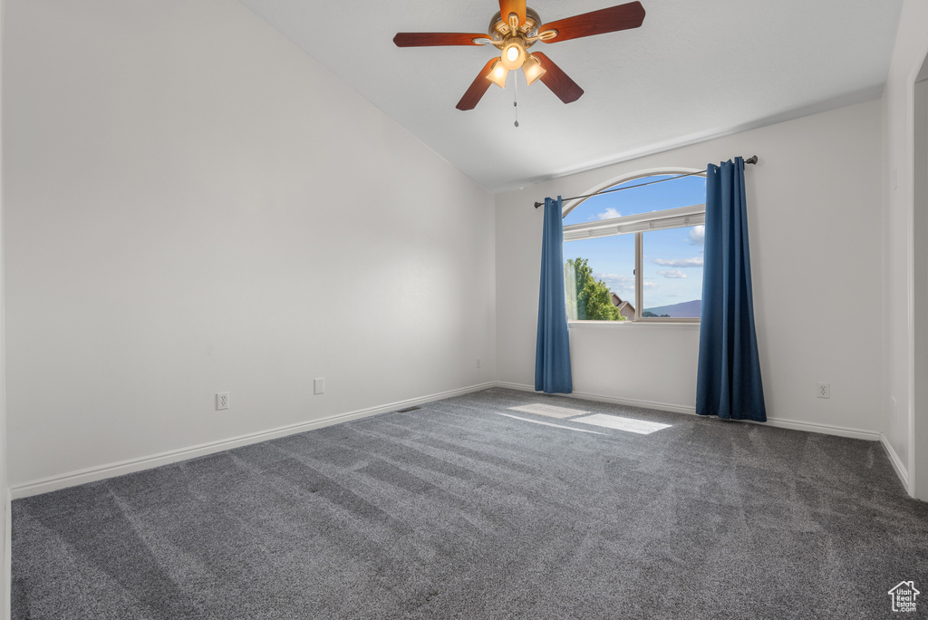 Carpeted spare room featuring vaulted ceiling and a ceiling fan