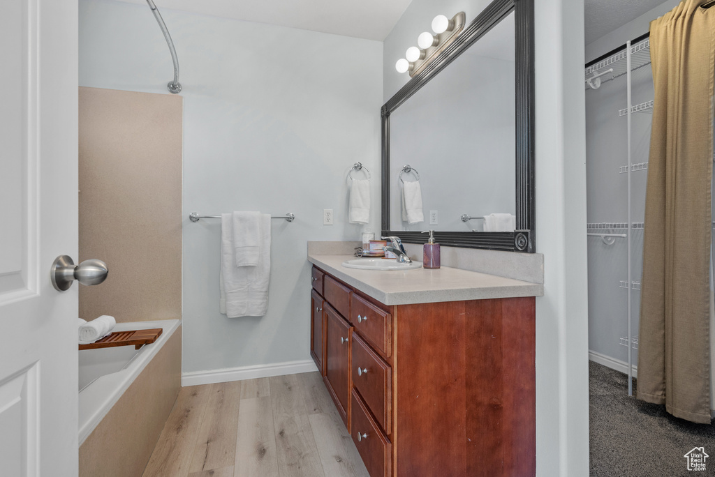 Bathroom with vanity, wood finished floors, a bathtub, and a walk in closet
