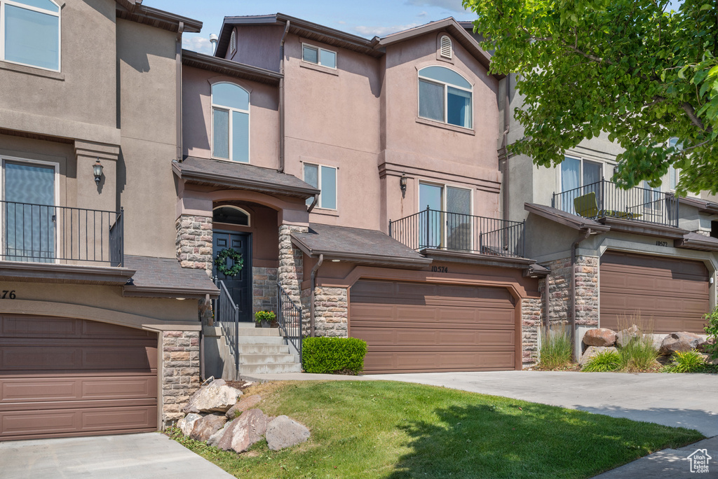 Multi unit property with stone siding, a garage, a balcony, and driveway