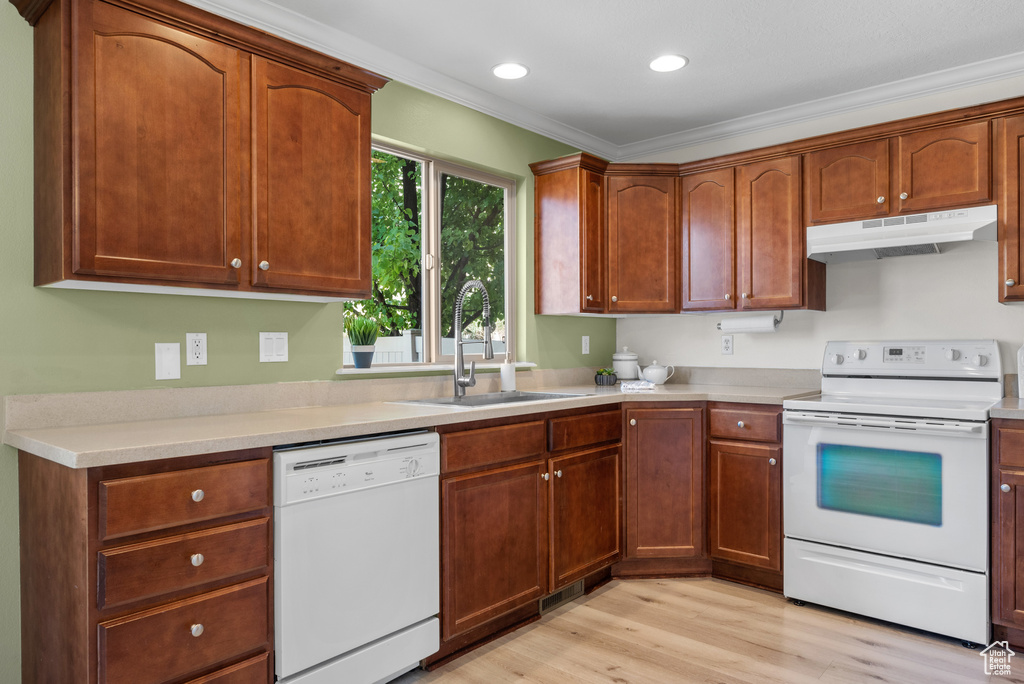 Kitchen with white appliances, under cabinet range hood, light wood-style floors, light countertops, and ornamental molding