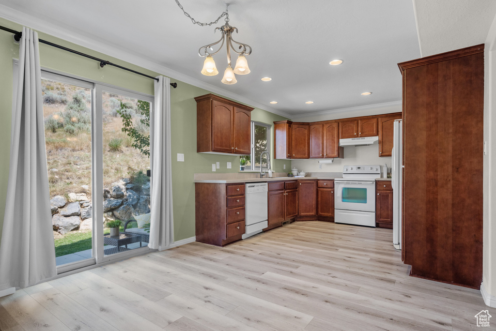 Kitchen with white appliances, under cabinet range hood, plenty of natural light, light countertops, and crown molding