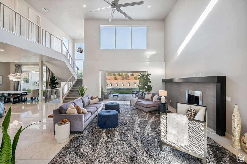 Living area featuring a ceiling fan, stairway, a towering ceiling, a fireplace, and recessed lighting