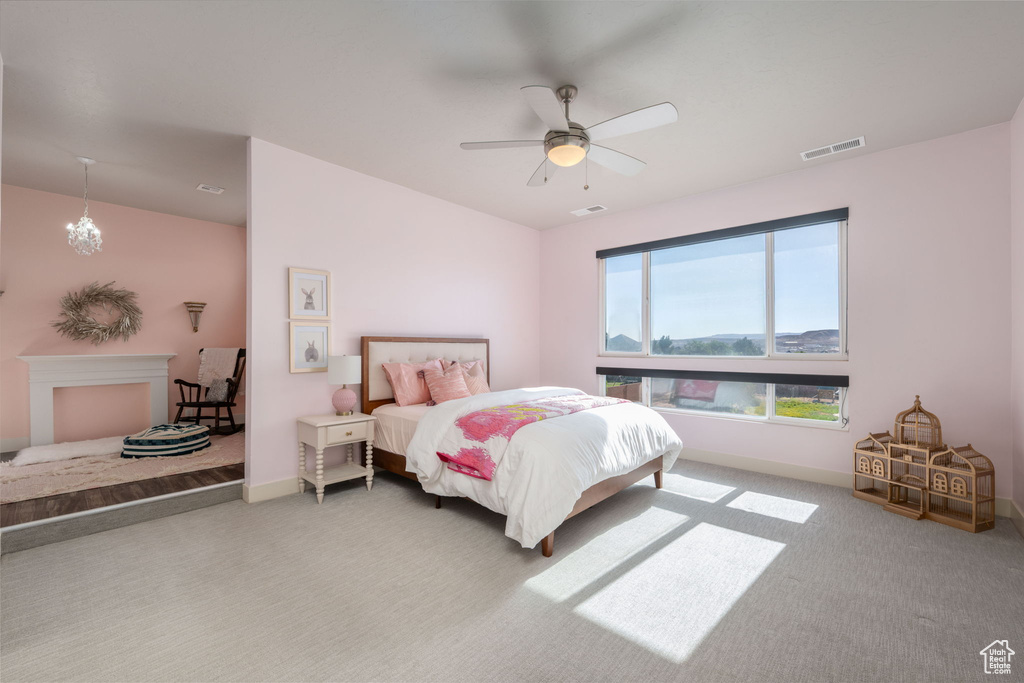 Carpeted bedroom featuring a ceiling fan and a chandelier