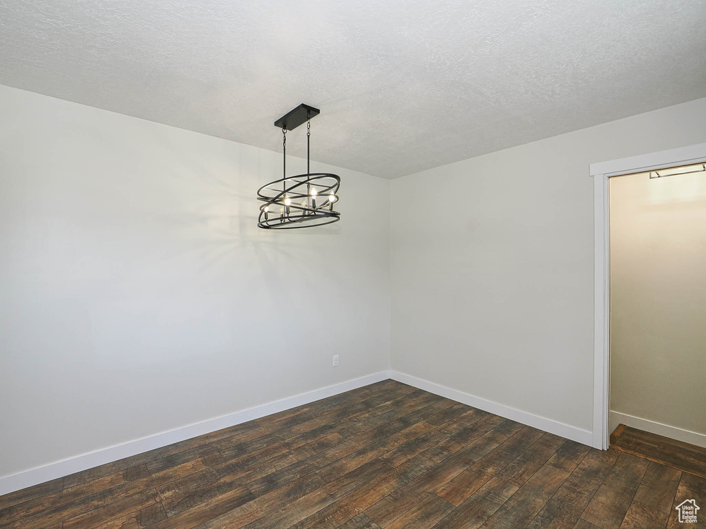 Spare room with dark wood finished floors, a textured ceiling, and a chandelier