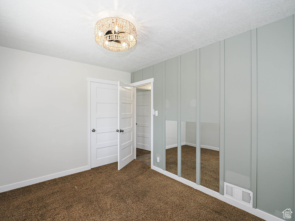 Unfurnished bedroom featuring dark carpet, a chandelier, and a textured ceiling