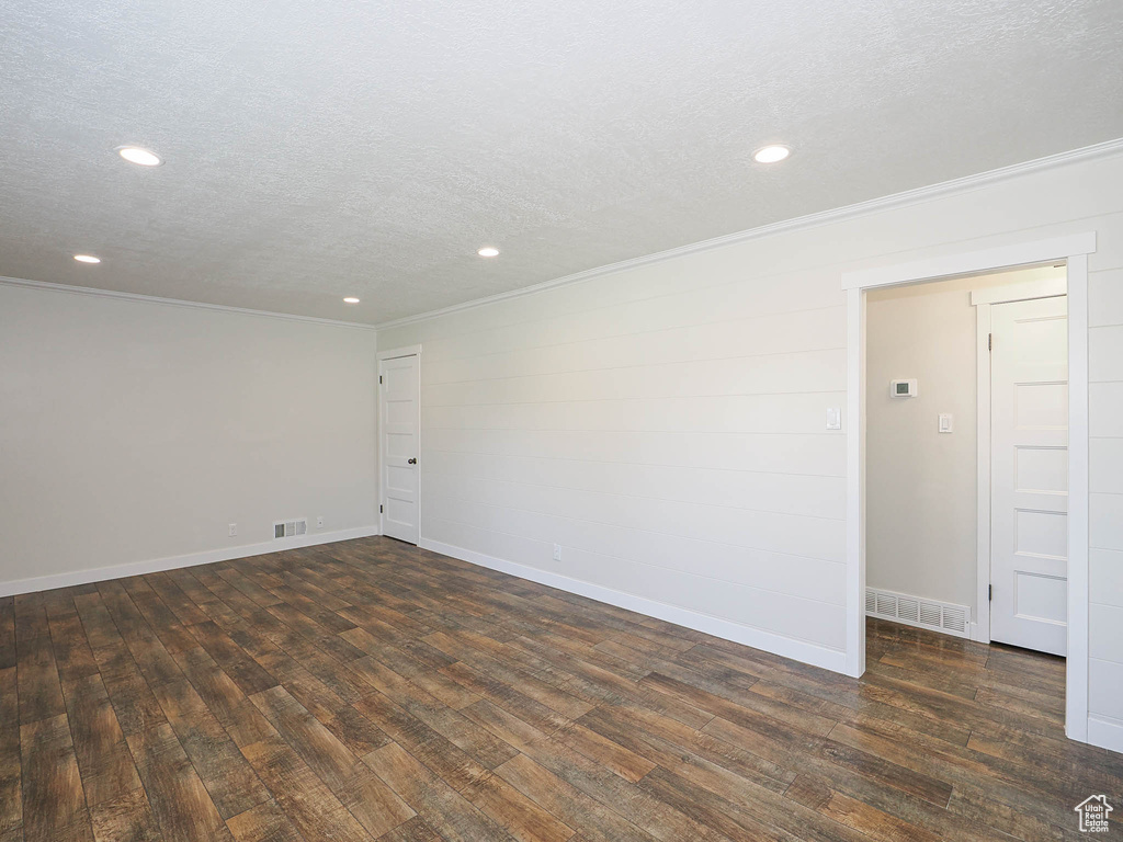 Empty room featuring a textured ceiling, dark wood-style flooring, crown molding, and recessed lighting