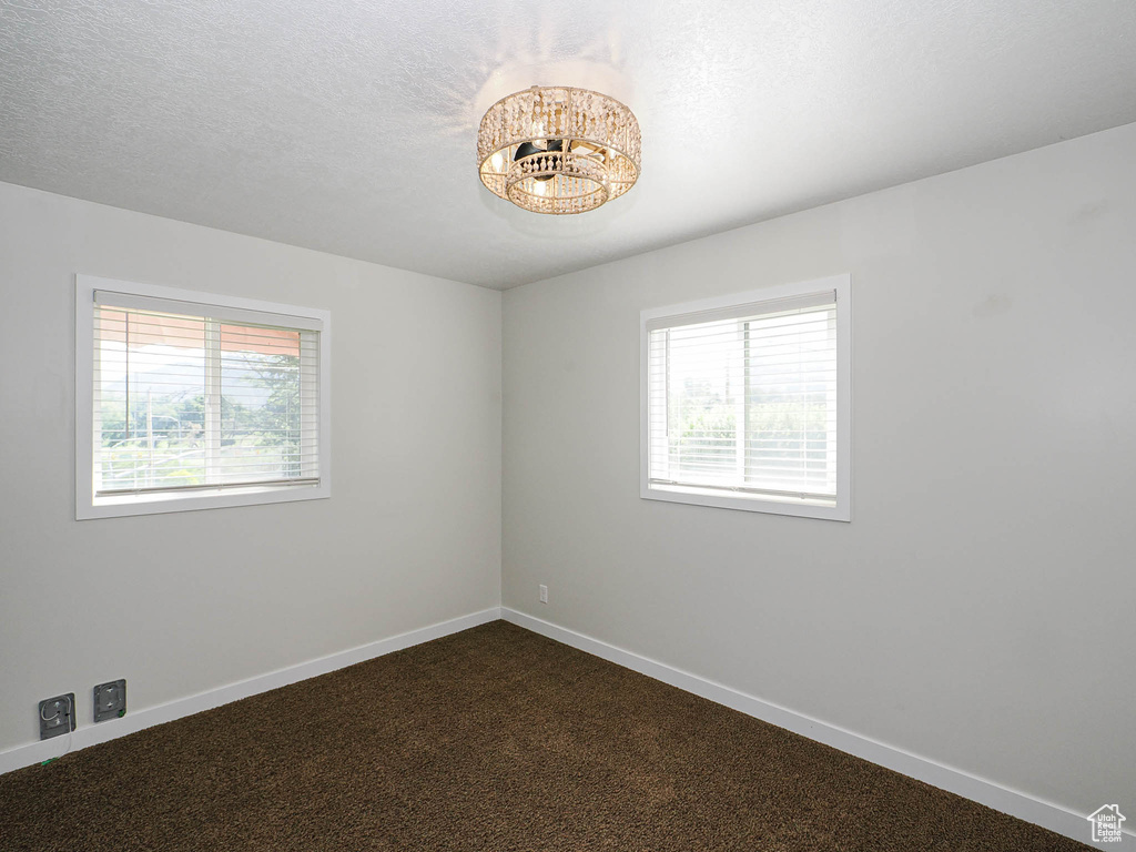 Spare room with dark colored carpet and a chandelier