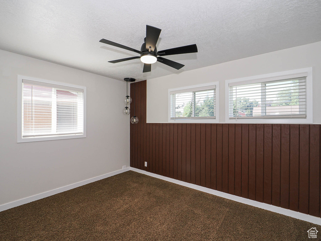 Empty room featuring a wainscoted wall, ceiling fan, wooden walls, a textured ceiling, and dark colored carpet