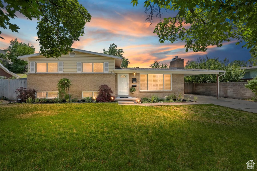 Split level home featuring a chimney, an attached carport, brick siding, and driveway