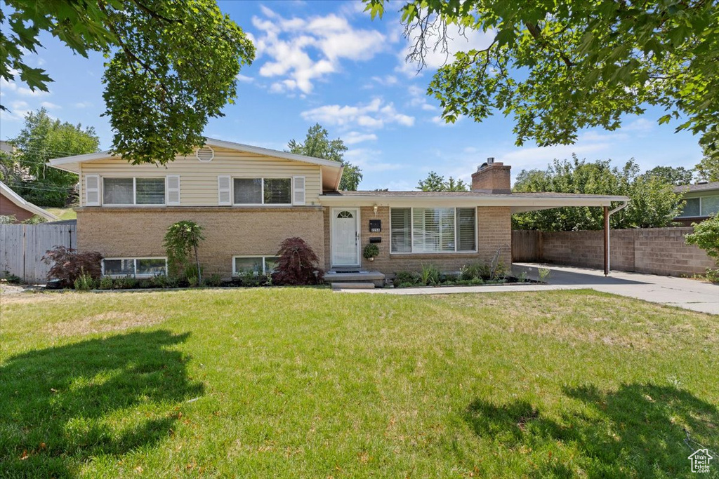Split level home with a chimney, a carport, concrete driveway, and brick siding