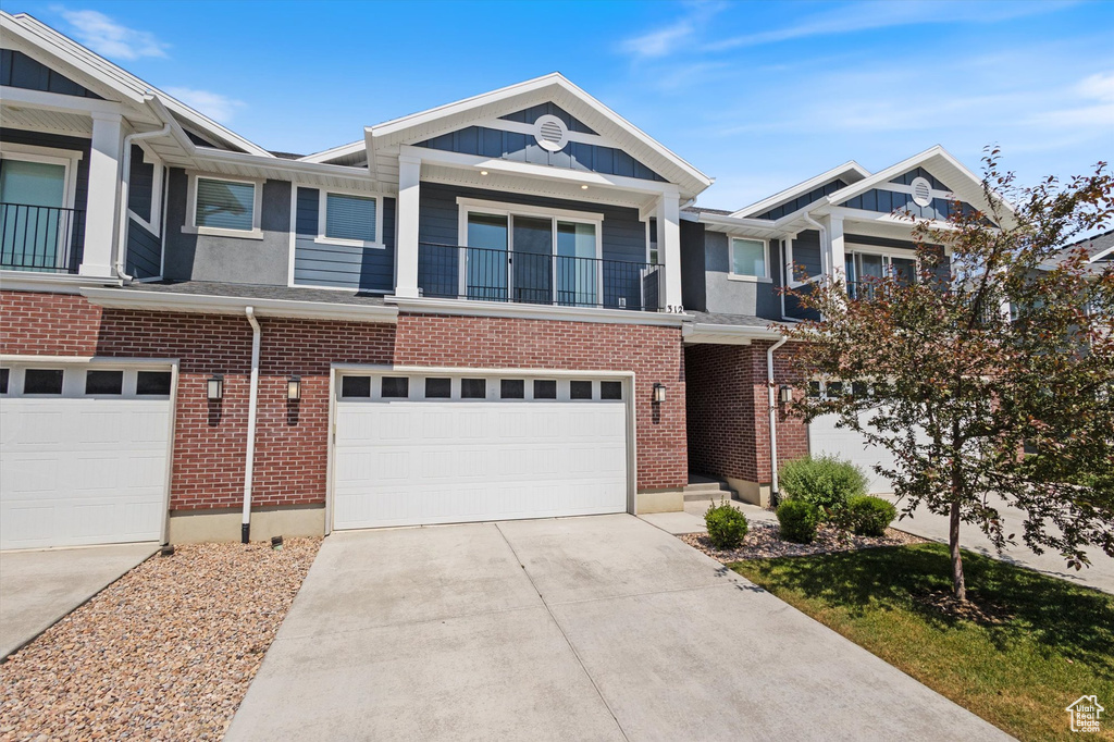 Multi unit property with board and batten siding, a garage, concrete driveway, a balcony, and brick siding