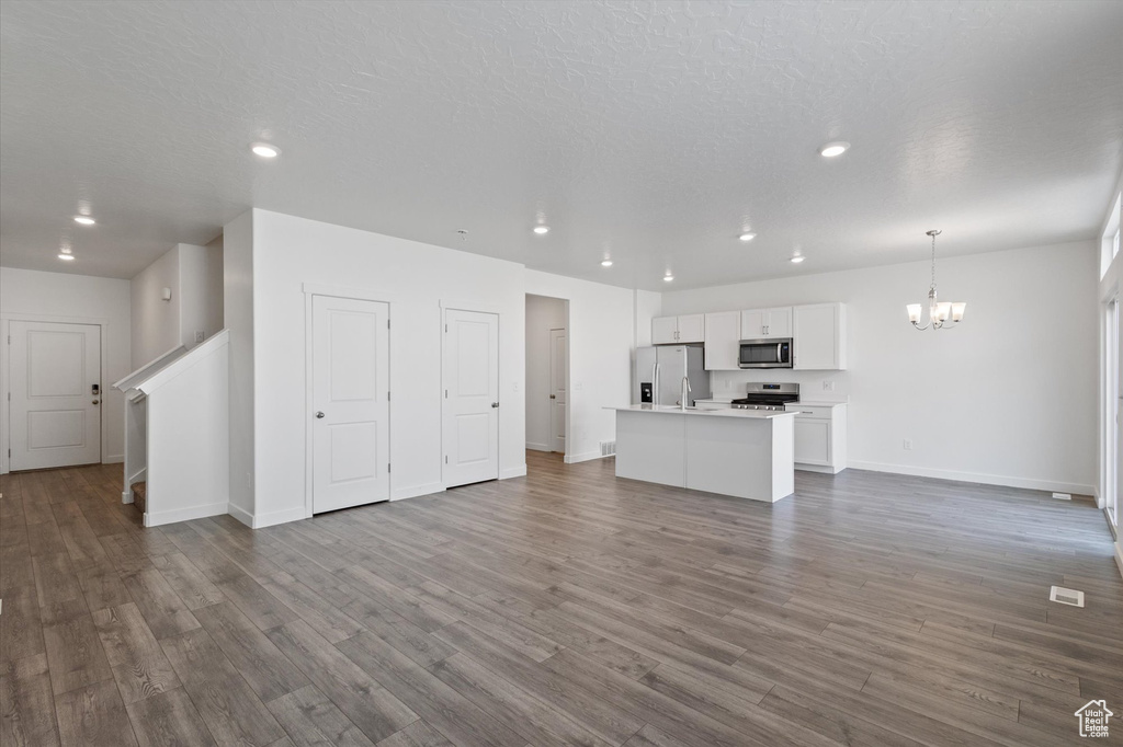 Unfurnished living room featuring a chandelier, recessed lighting, dark wood finished floors, and stairs